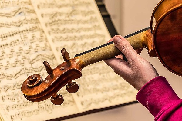 Detail einer Violine in den Händen einer jugendlichen Musikschülerin, im Hintergrund ein Notenblatt auf einem Notenständer